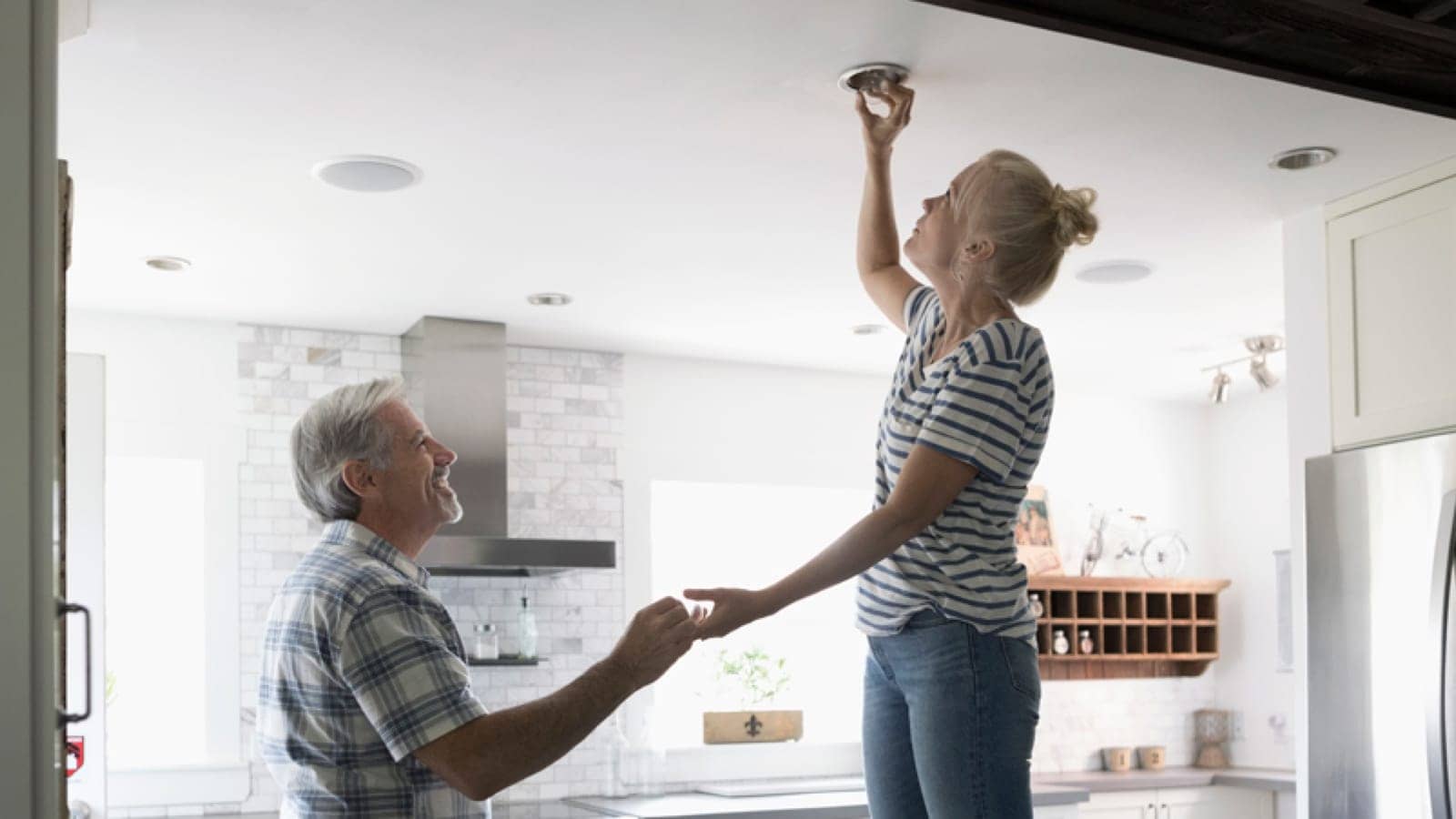 Older couple changing a lightbulb in their kitchen