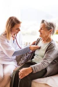 Health care worker examining senior patient during a home visit.