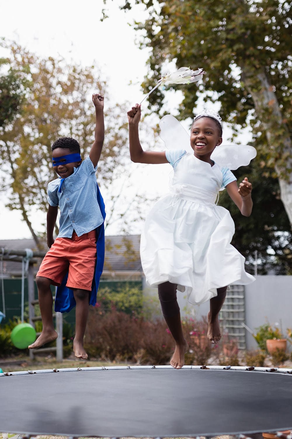 Kids jumping on a trampoline in the backyard of a residence.