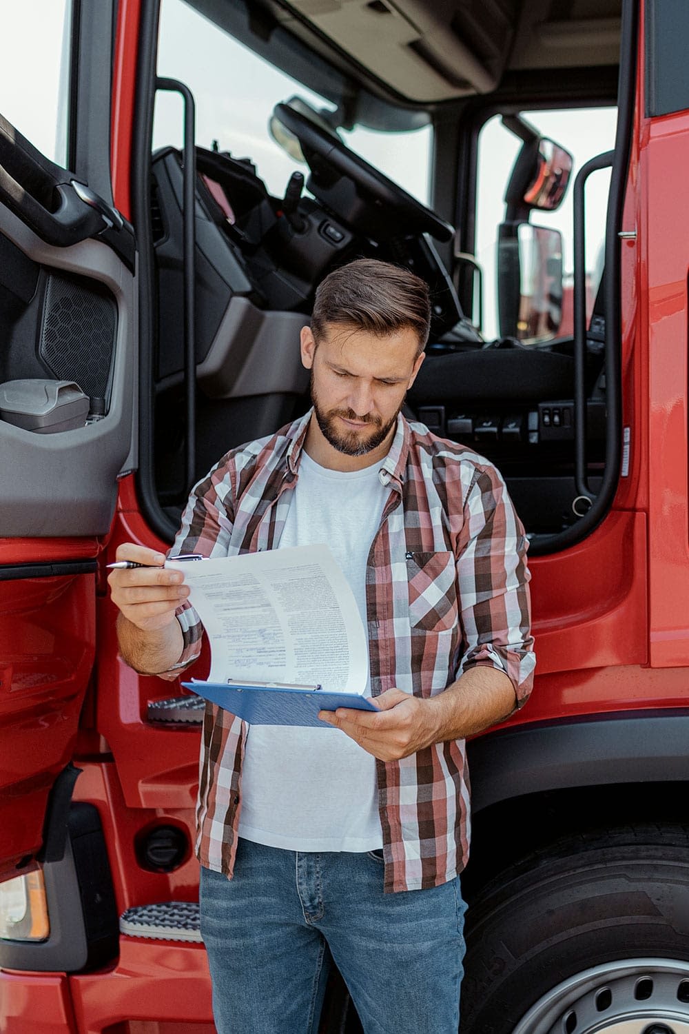 Truck driver reviewing paperwork outside open truck door.
