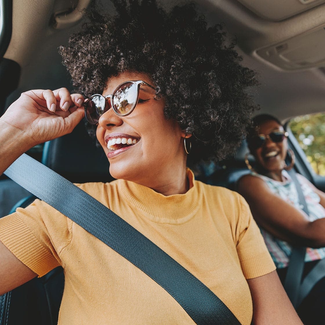 Happy woman with curly hair driving a car, with another smiling passenger in the background