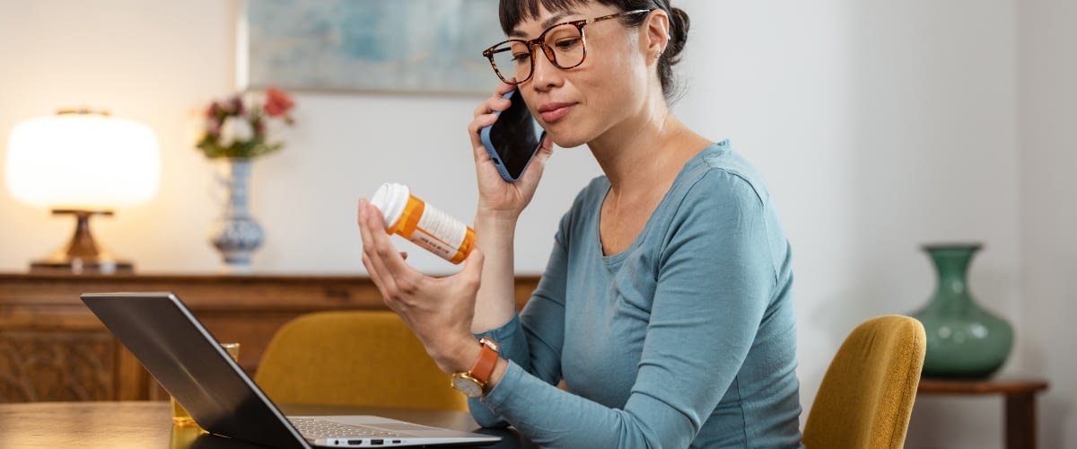 Woman holding prescription bottle while speaking on the phone.