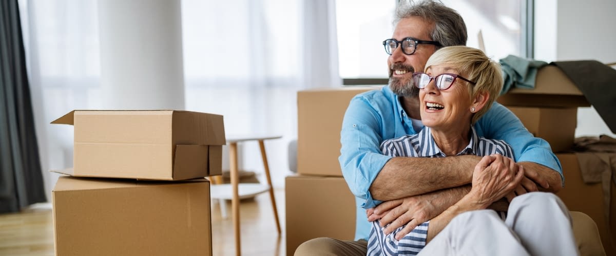 May 21 blog Older couple smiling in new home with moving boxes.