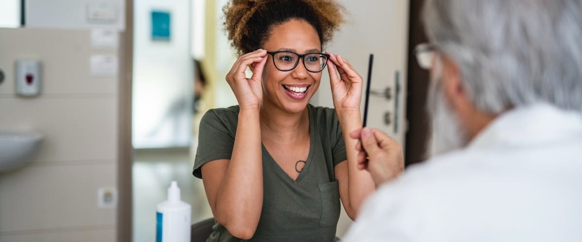 May 13 blog Young woman trying on new glasses at eye doctor.