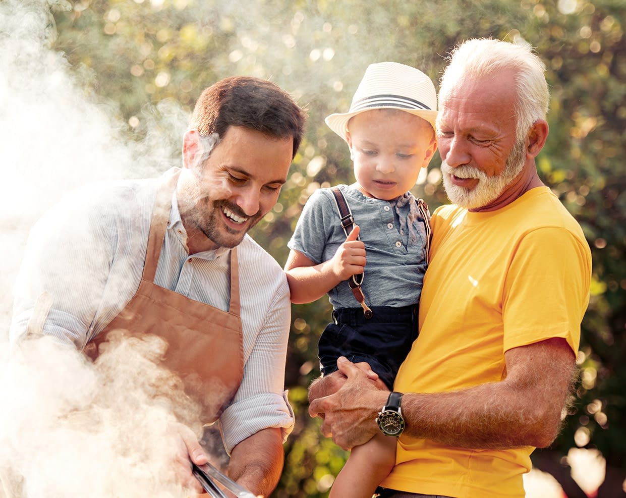 a grandfather carrying his grandson looking at his son grilling