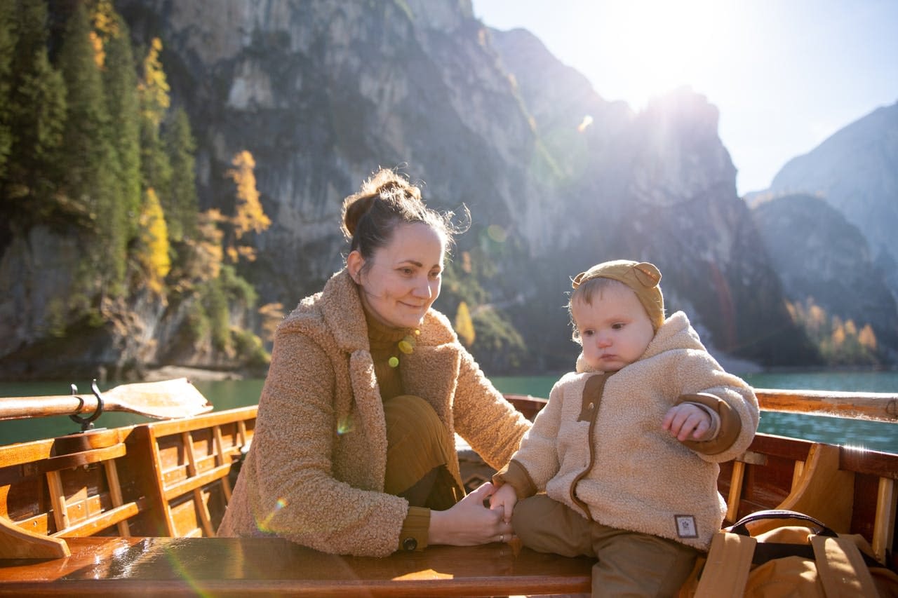woman-in-brown-sweater-sitting-on-brown-wooden-boat-with-baby