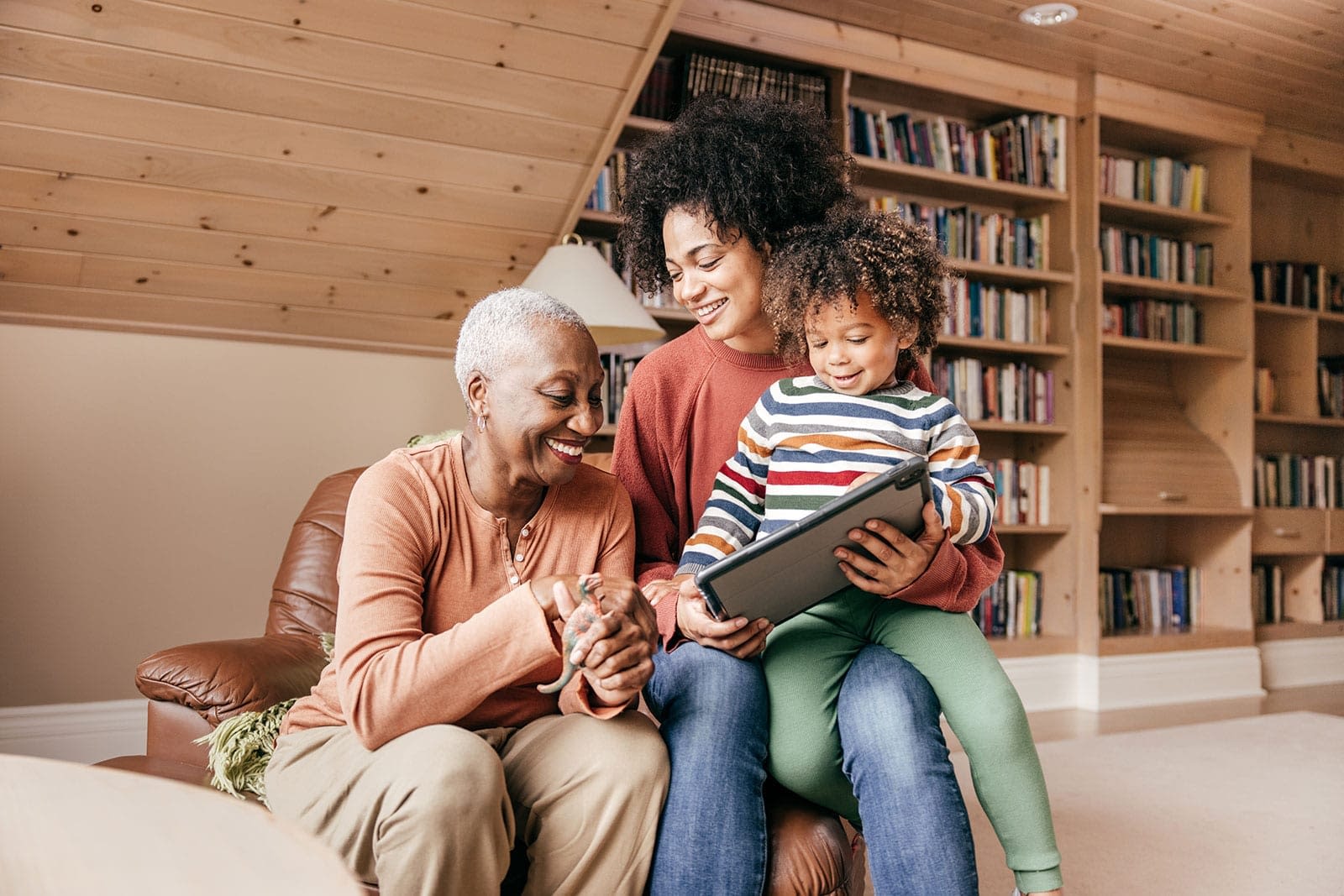 A grandmother, mother, and young child sitting together in a library and looking at a tablet.