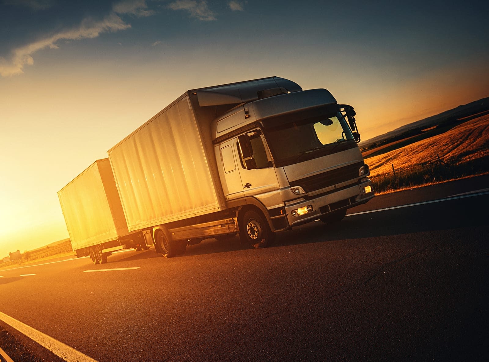Closeup front view of a white double truck driving on a highway. It's summer sunset and the sunlight is coming behind rear part of the tank. Low angle shot, tilt. Brand and logo free.