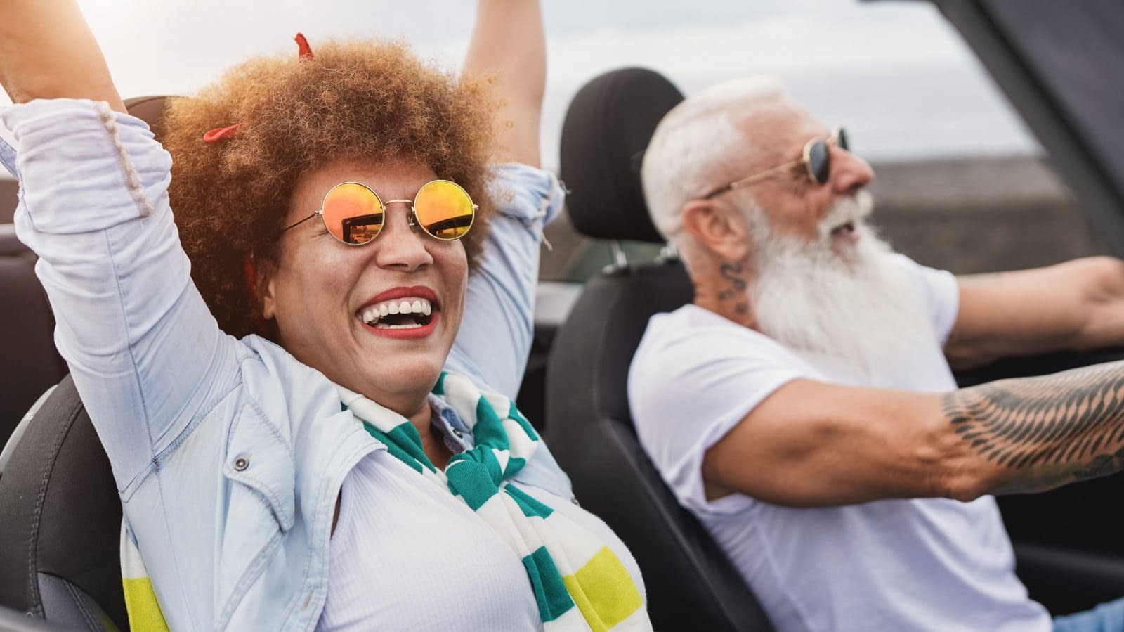 Trendy senior couple having fun inside convertible car – Multiracial mature people on a road trip with cabriolet car Senior Couple riding in car