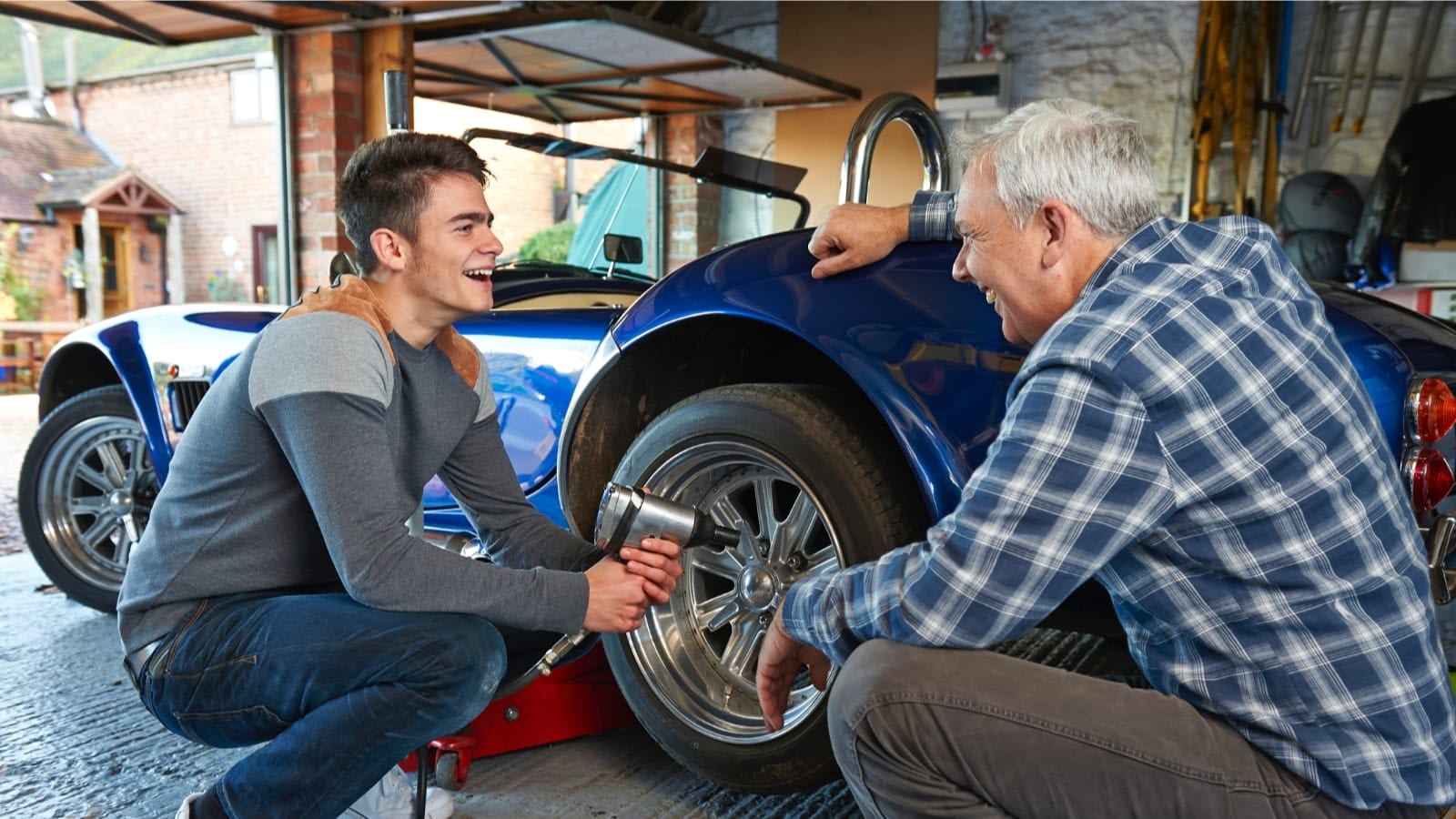 father and adult son changing a tire on a 1965 Shelby Cobra
