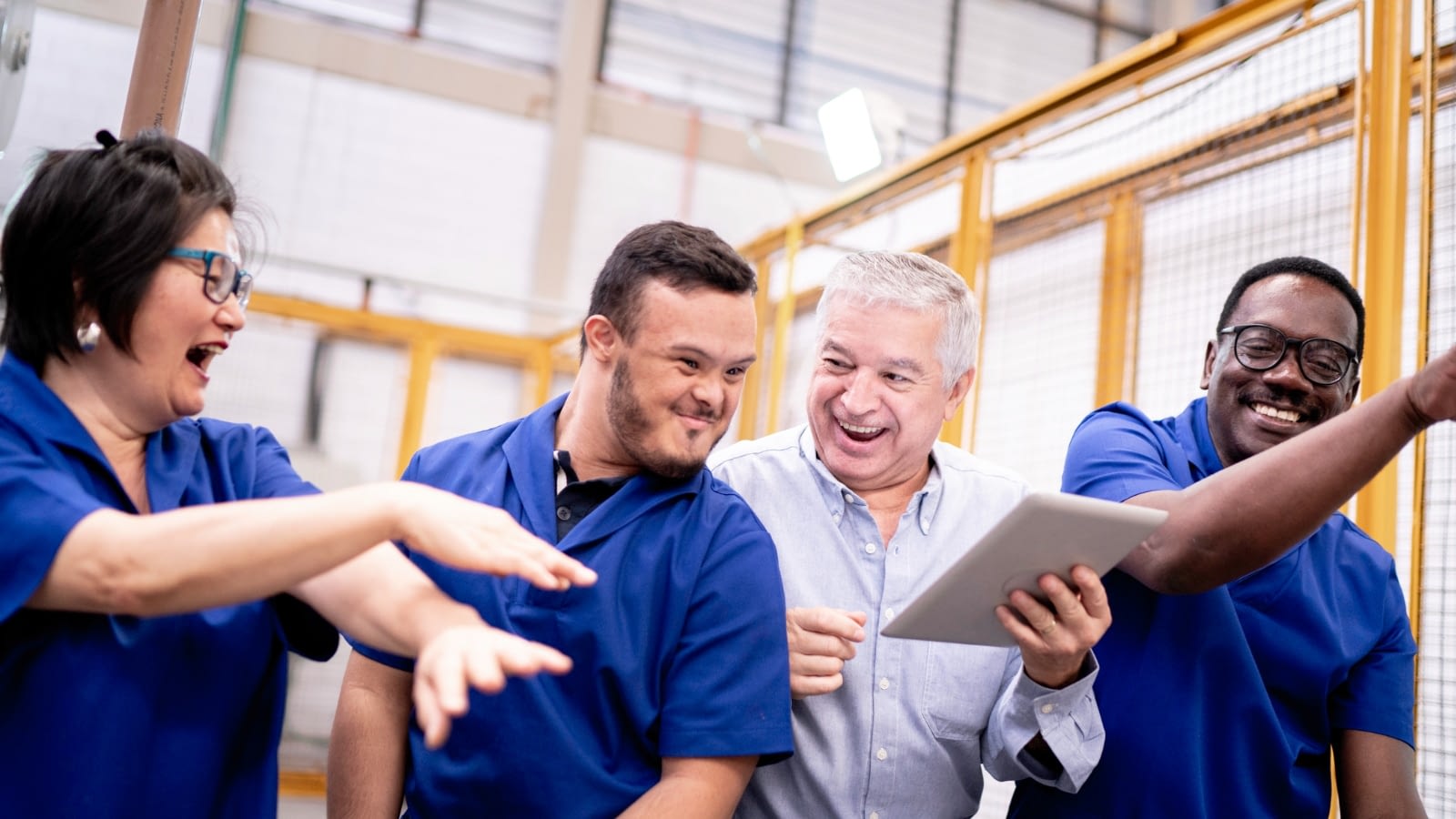 Group of blue-collar employees dancing and laughing with mentally disabled co-worker.