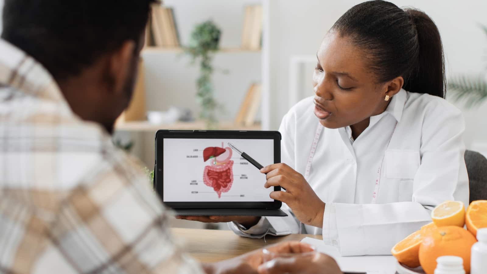 Female African-American doctor pointing to iPad with diagram of human gut on it talking to male patient