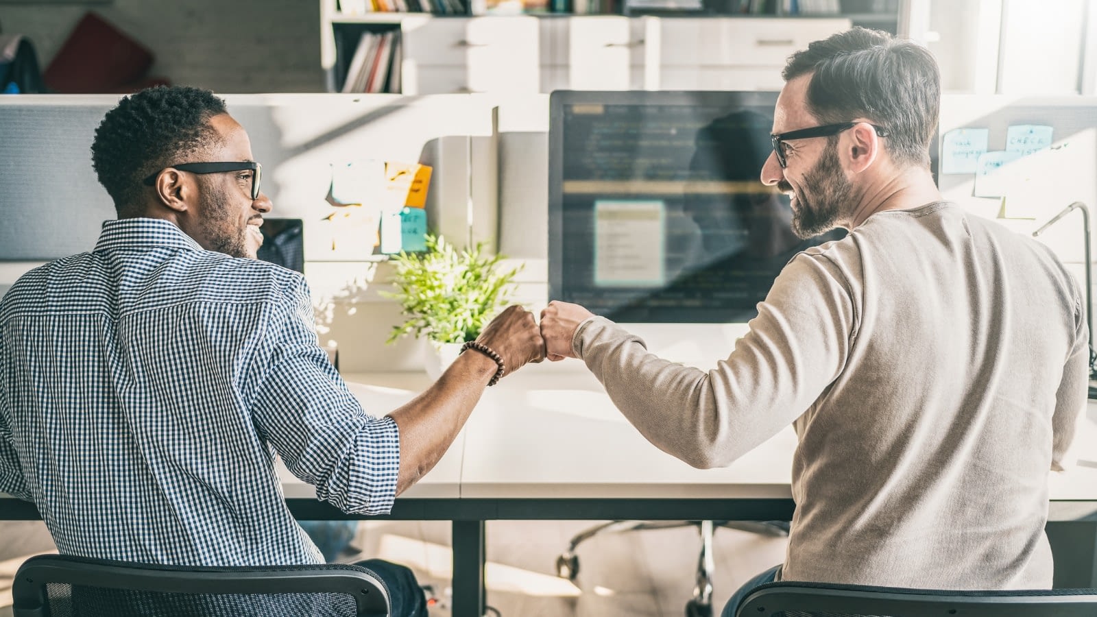 two male employees fist-bumping at their work desks