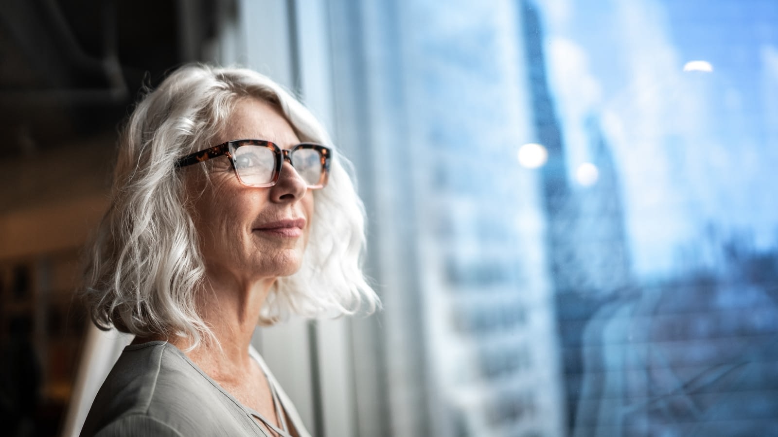 Older woman smiling while deep in thought looking out window.