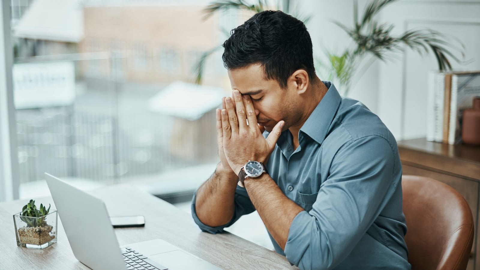 Young man with face buried in hands at desk stressed at work.