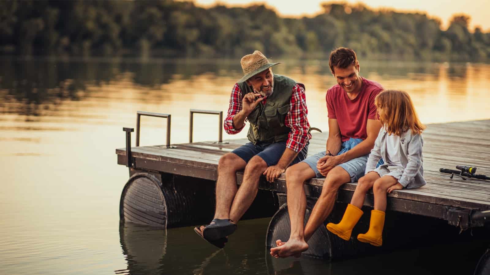 Father, grandfather, and daughter sitting on dock at sunset