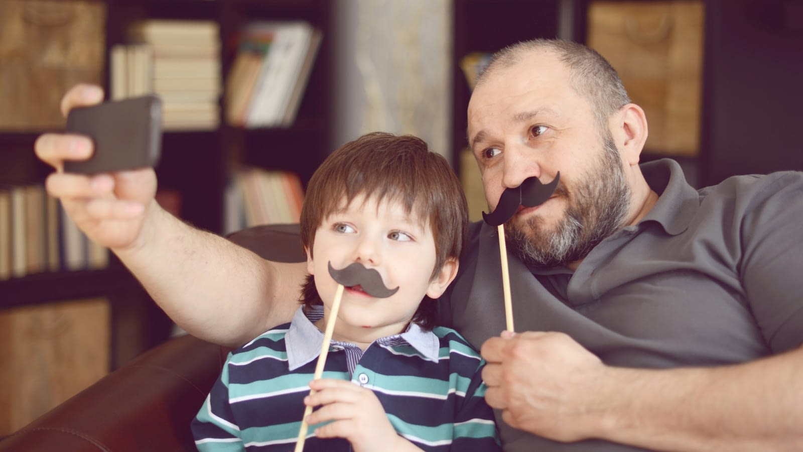 father and son taking a picture with mustache props