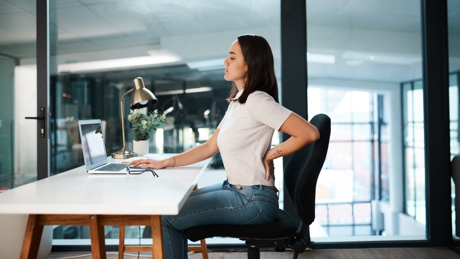 young woman experiencing back pain sitting at her desk