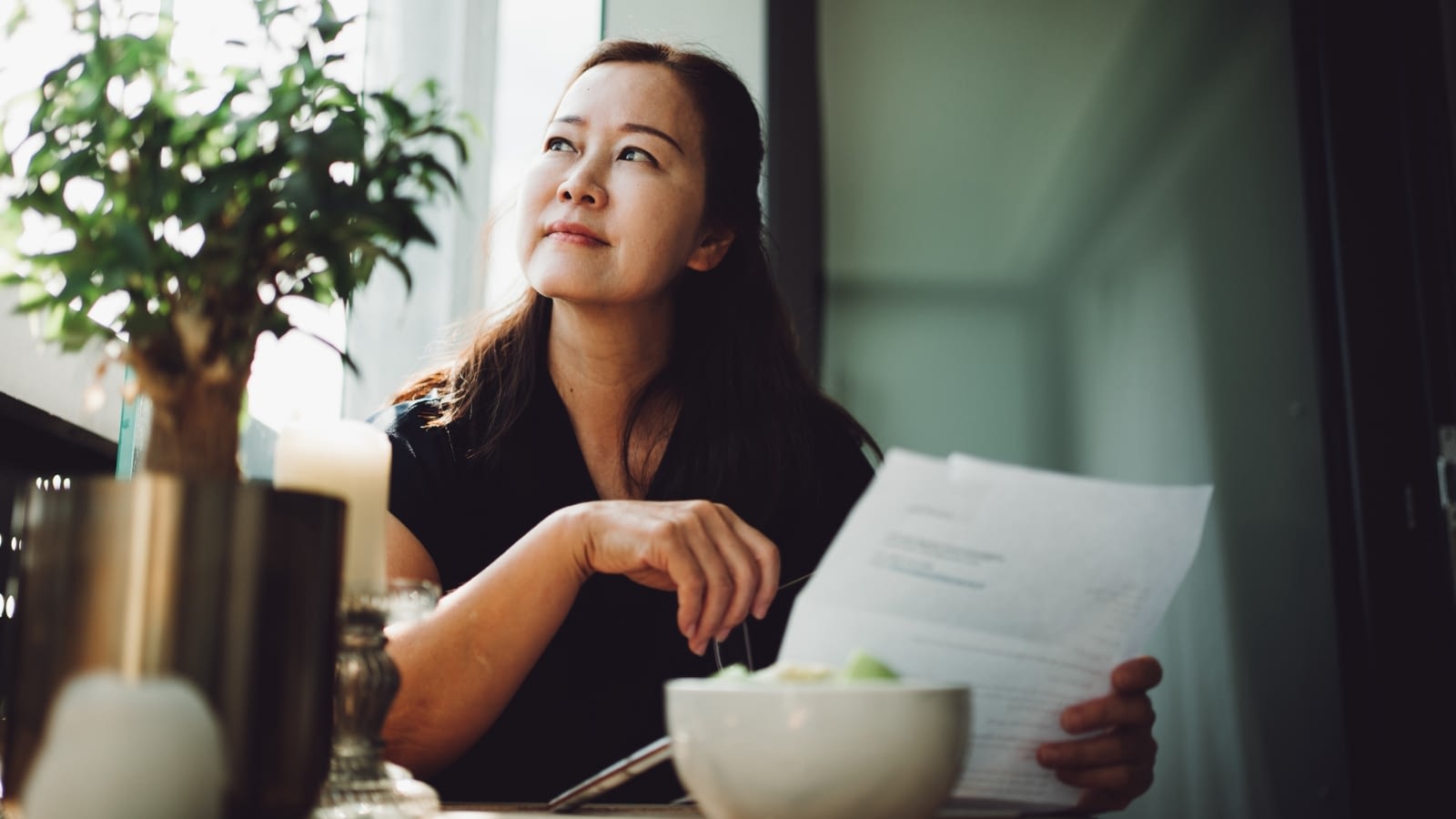 Asian woman looking up in deep thought from life insurance paperwork.