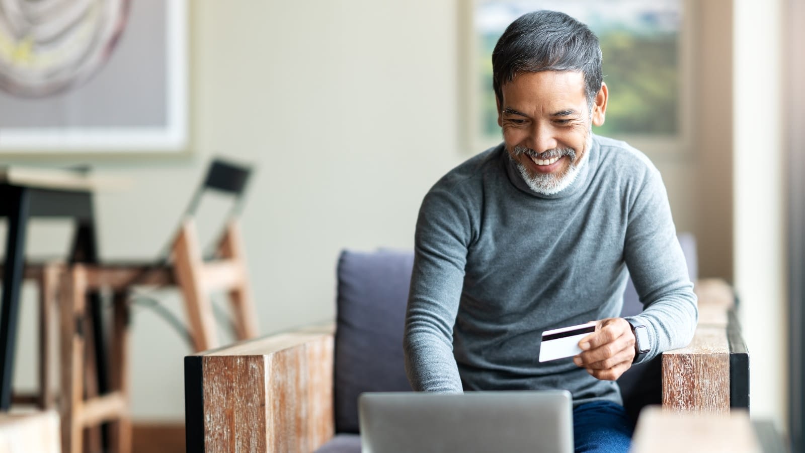 Man looking at computer and holding a card Senior man on the computer