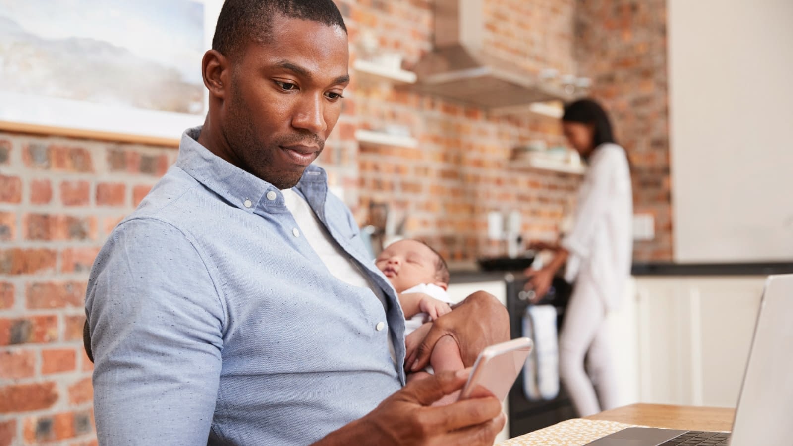 May 22 blog Young African American father reading something on his phone with family in background