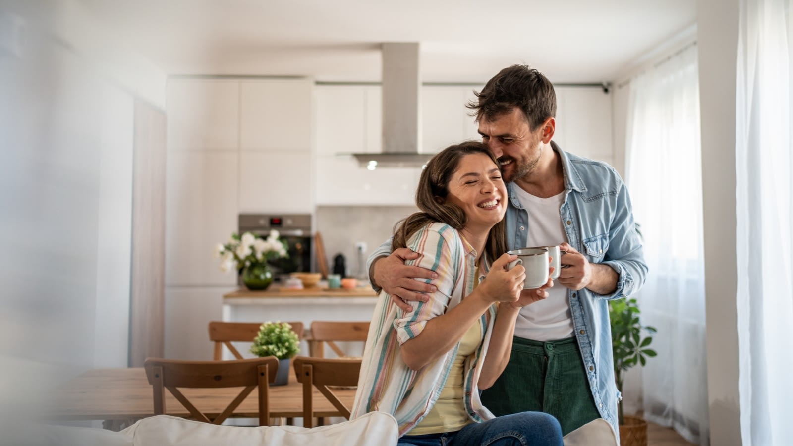 Happy young couple hugging and smiling while holding coffee cups.