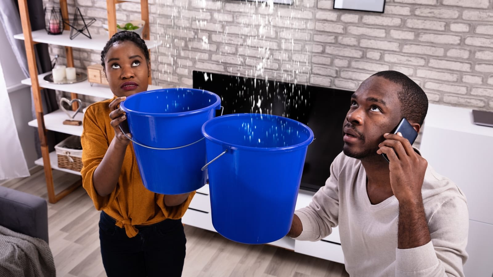 Couple holding buckets under a leaking ceiling