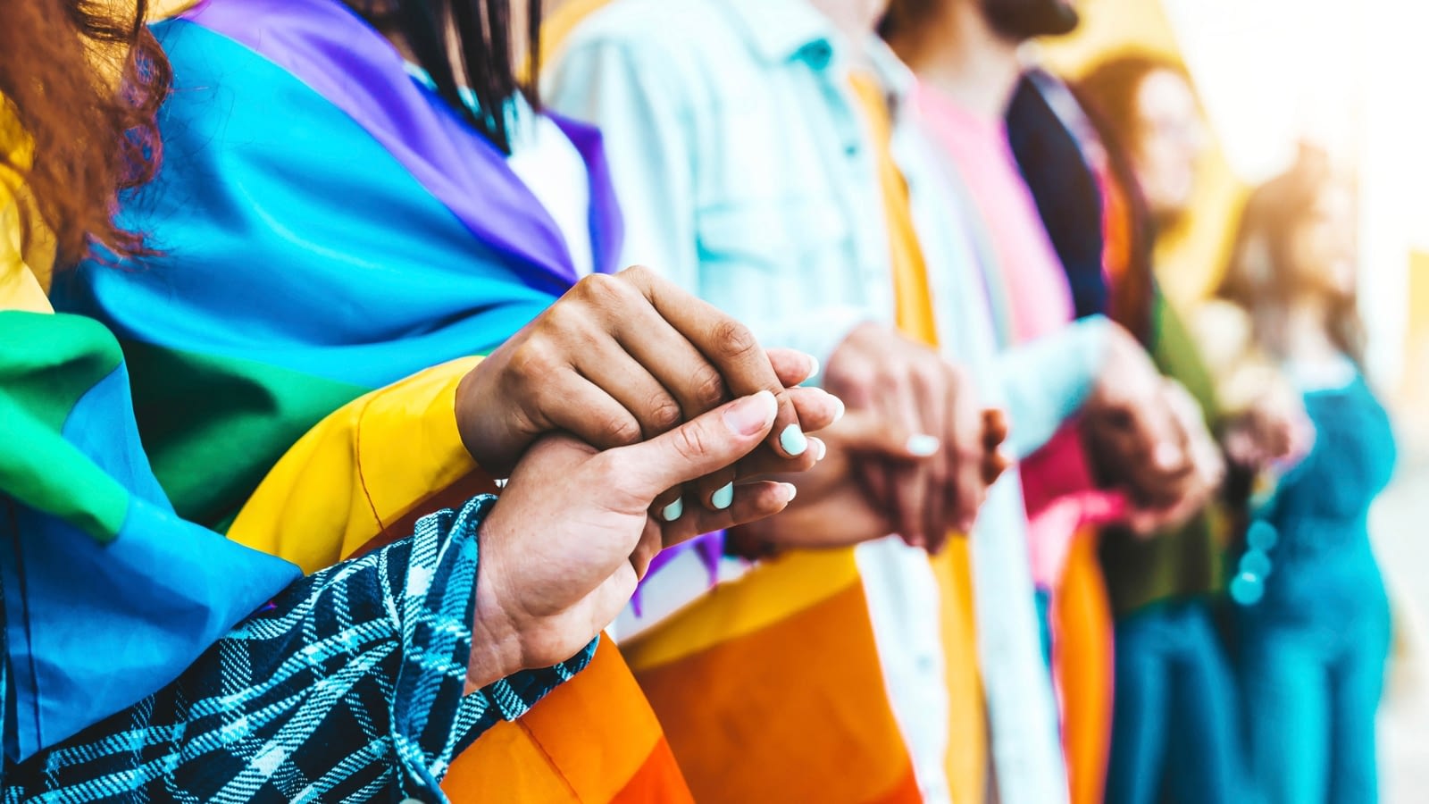 group of people holding hands wearing pride flags