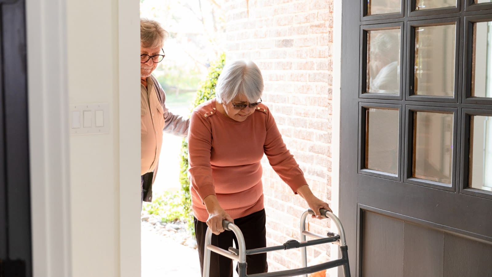 Feb 21 Elderly woman with a walker being helped inside her home.