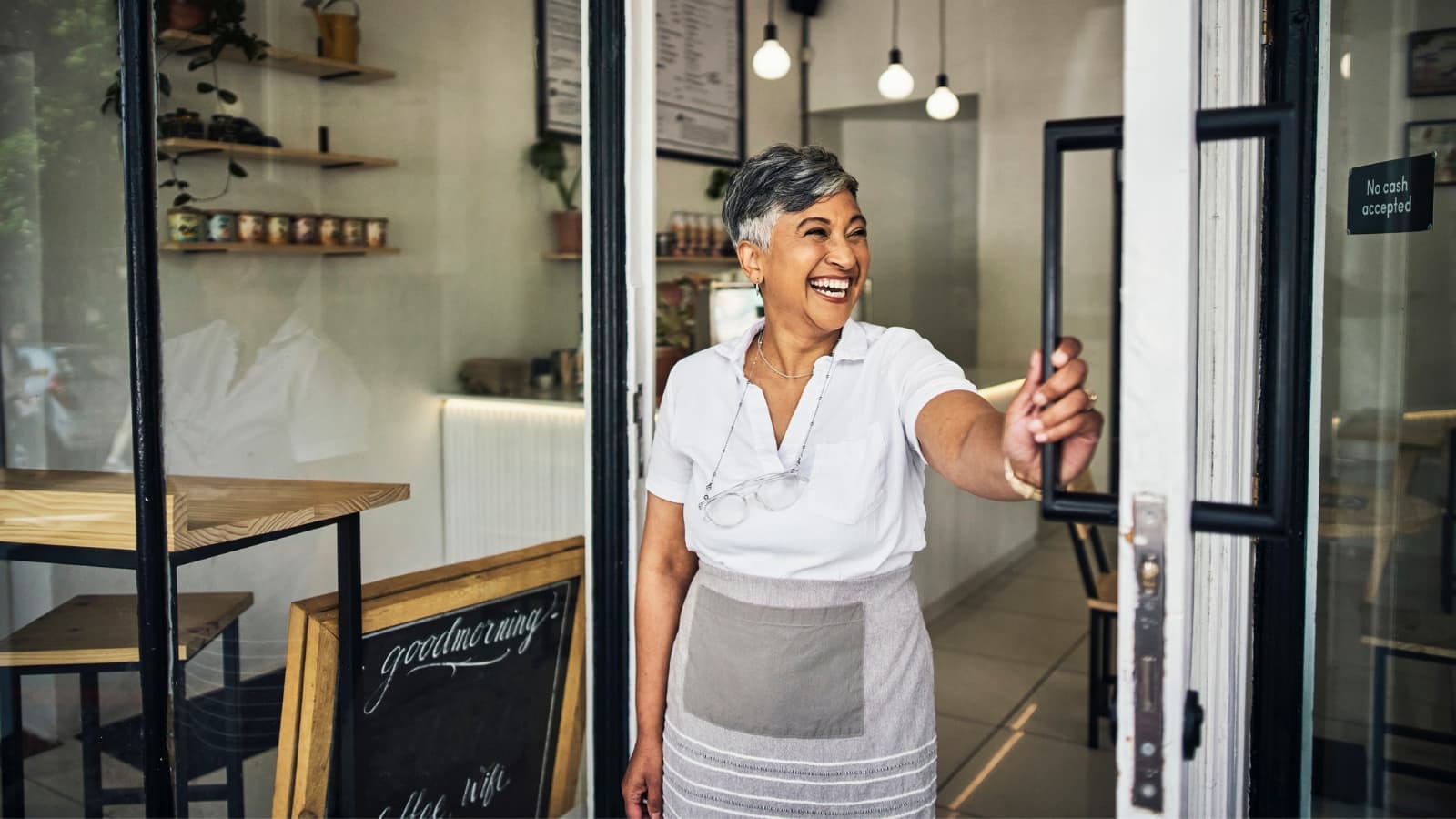 African-American female business owner opening door to cafe and smiling.