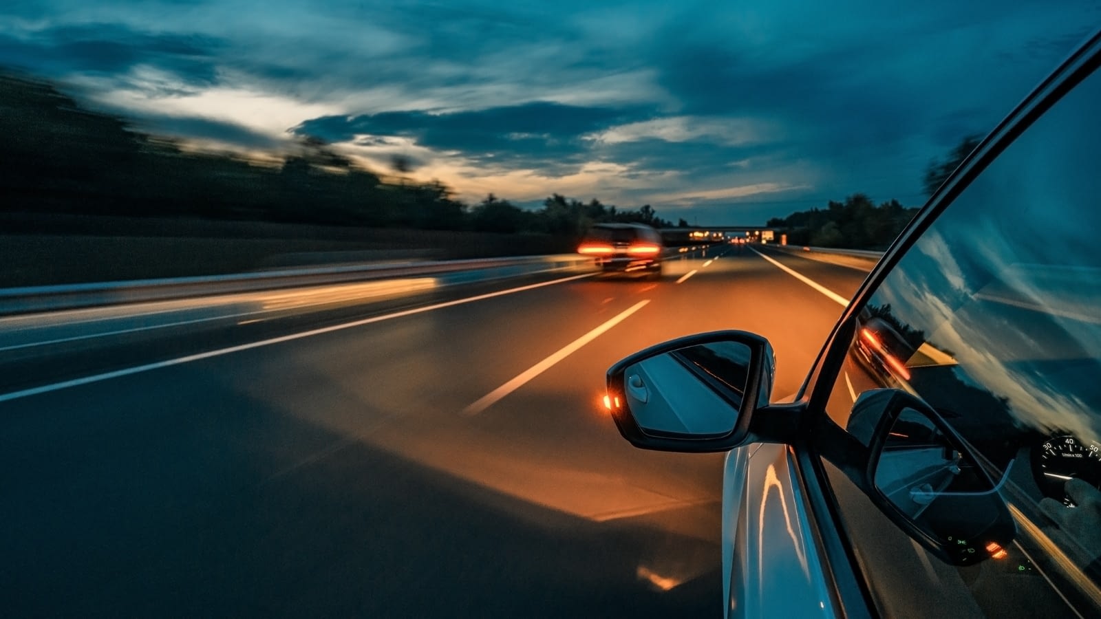 Close-up of car exterior front side mirror while driving at dusk.