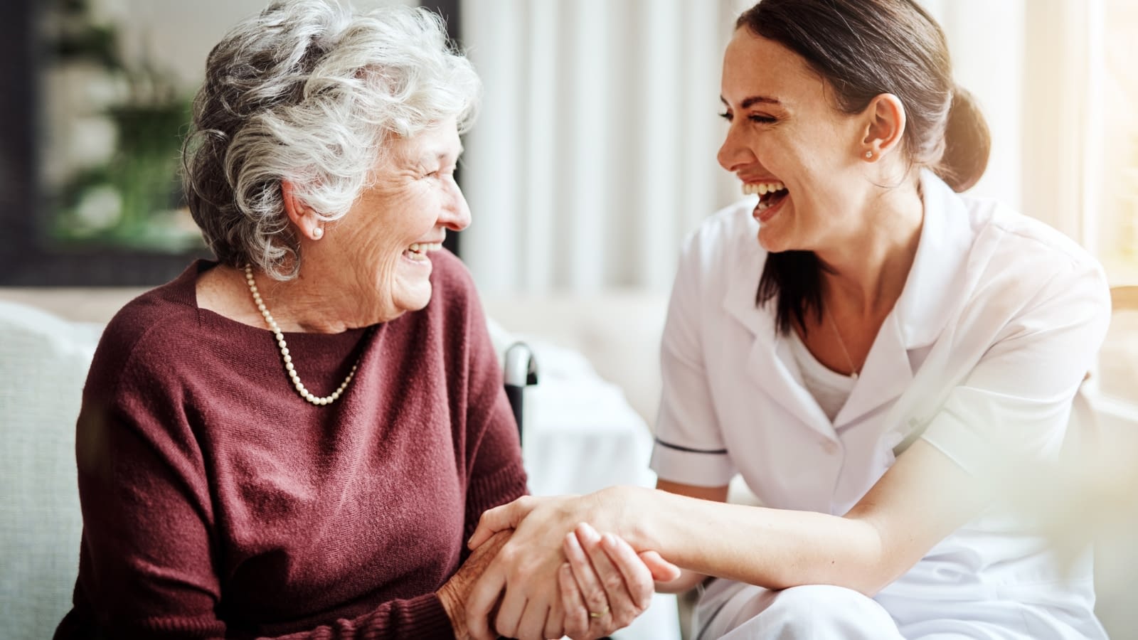 dual eligible elderly woman and caregiver laughing and holding hands