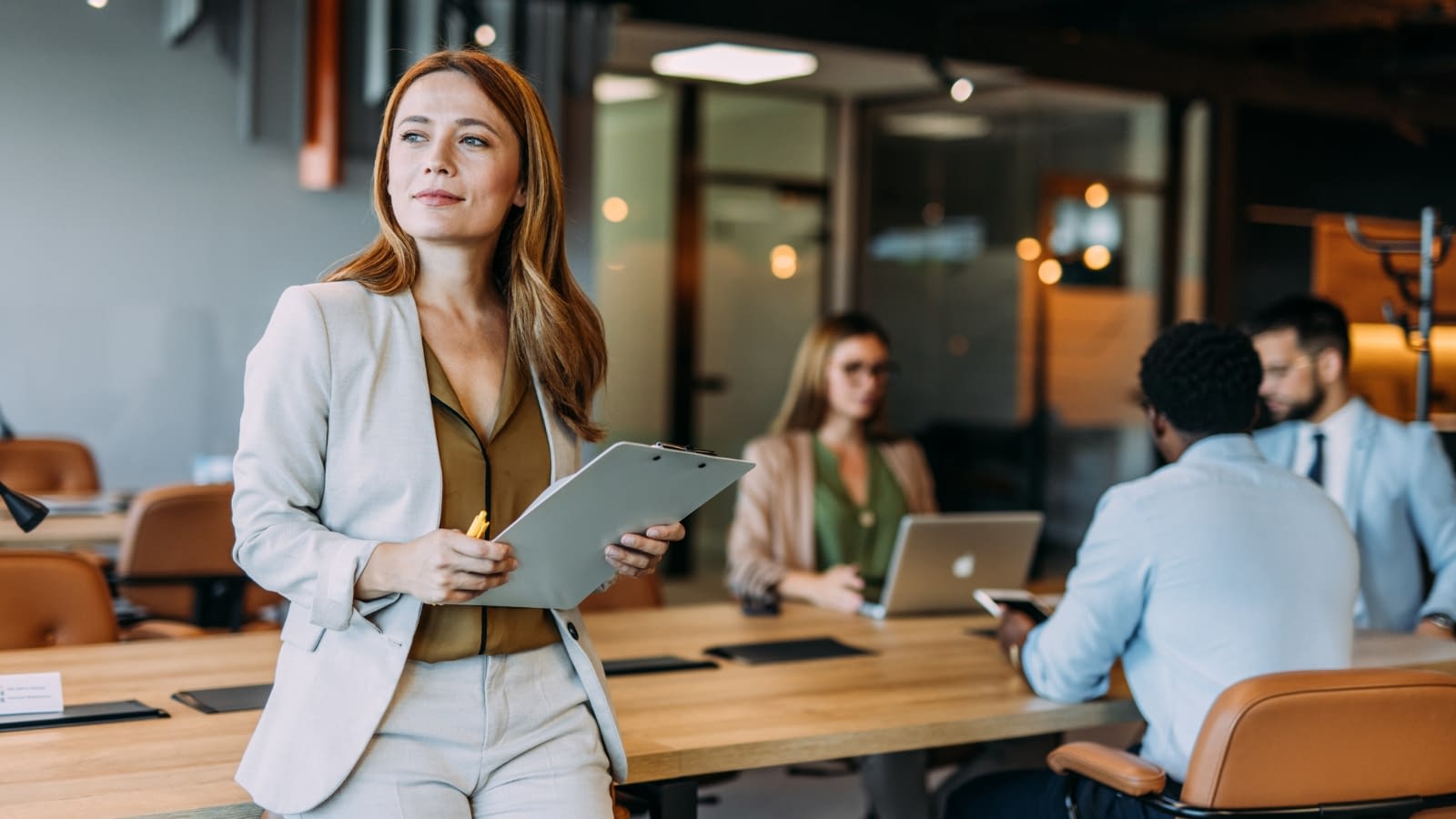 April 13 blog Young woman thinking to herself in conference room with coworkers in background.