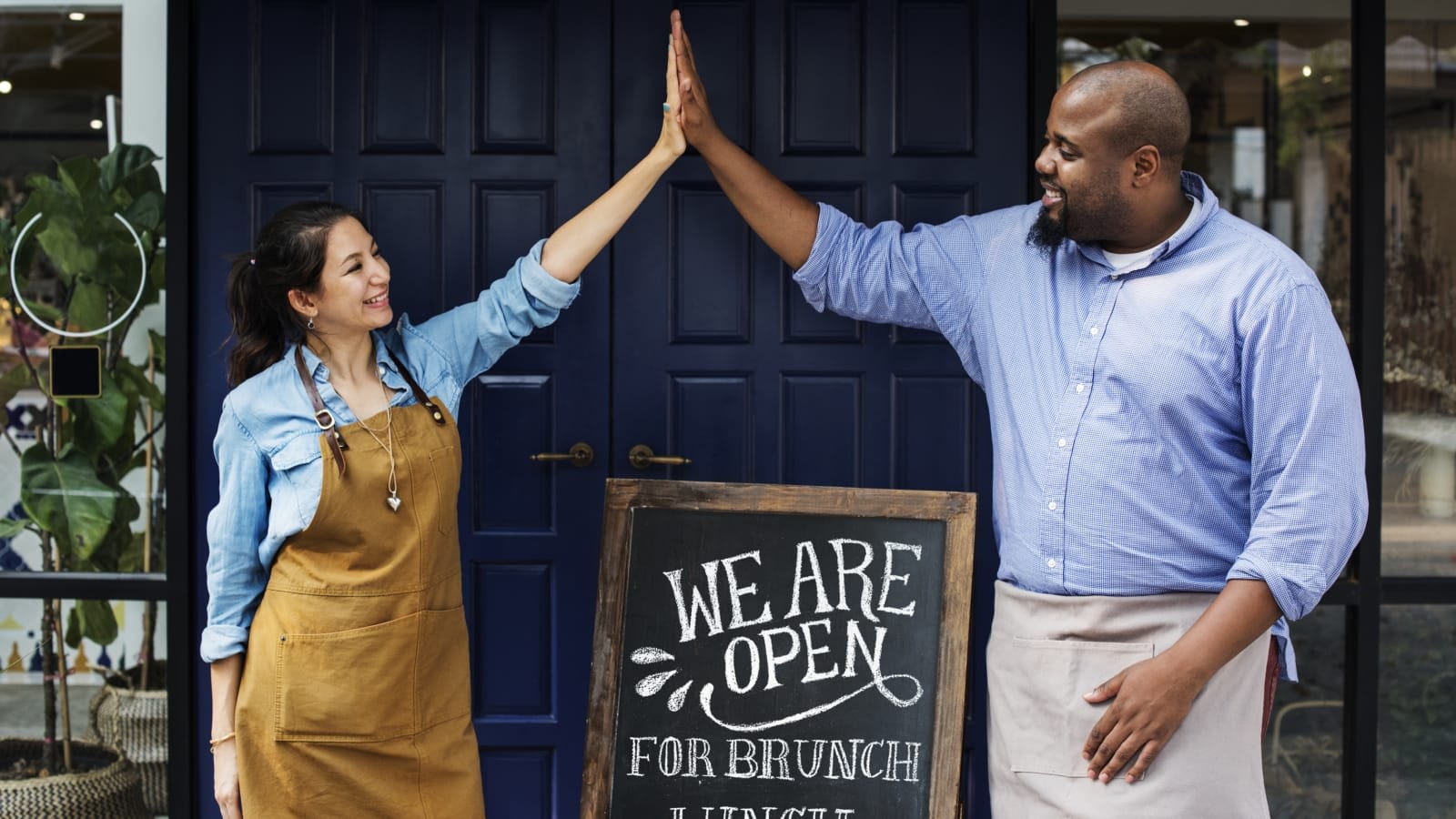 Cheerful business owners standing with open blackboard