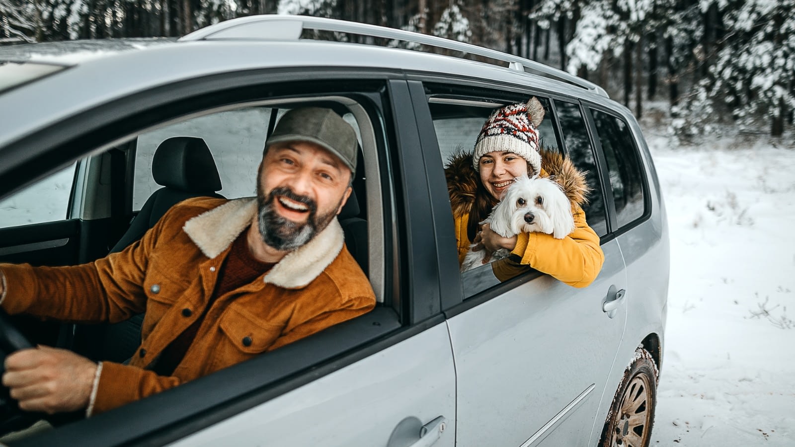 father driving in the snow with his daughter and dog in the back seat