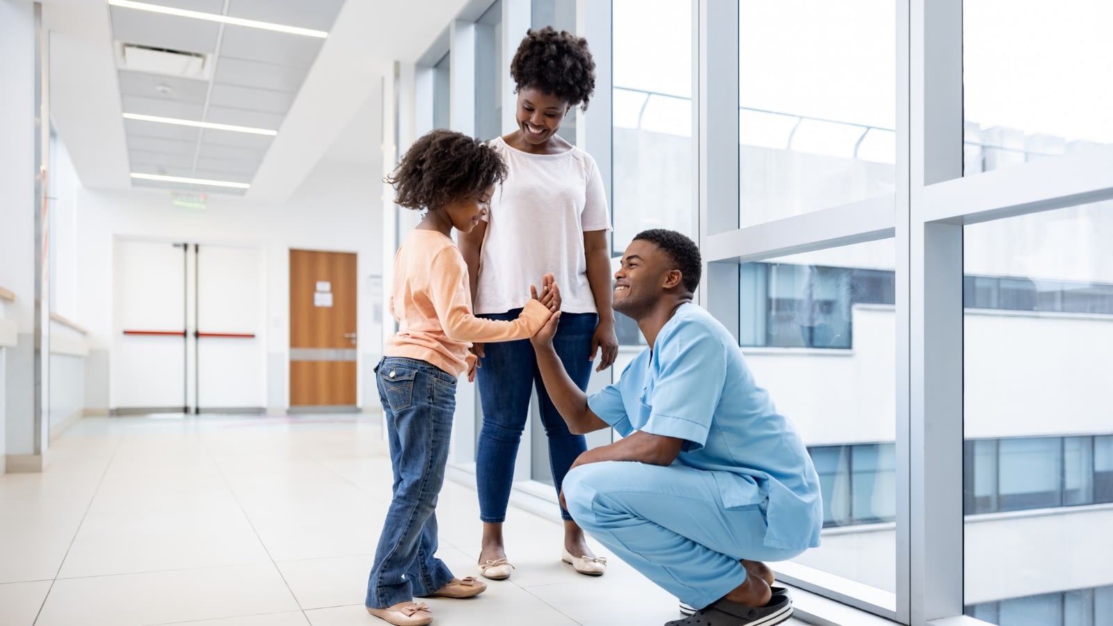 young male doctor giving high five to little girl standing with her mom