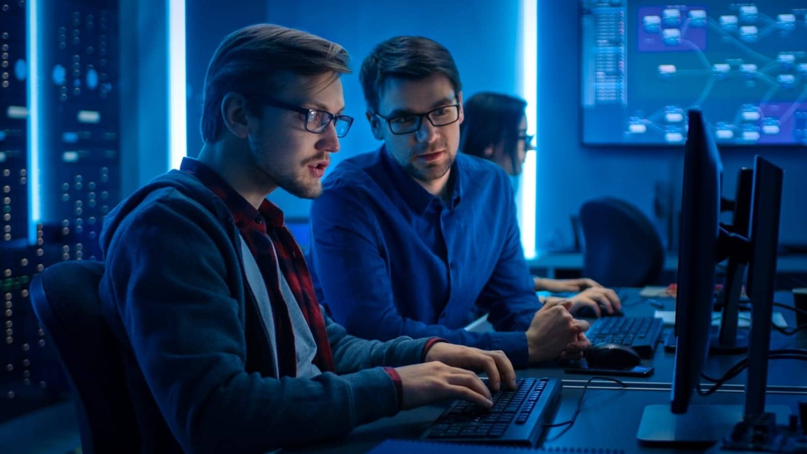 two men in the technology industry looking at a computer screen in a dark blue tinted room