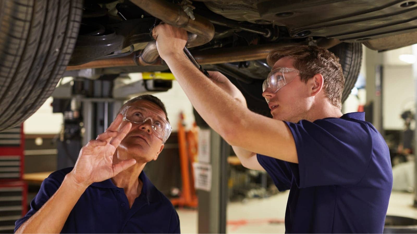 two garage technicians working on a cars exhaust system