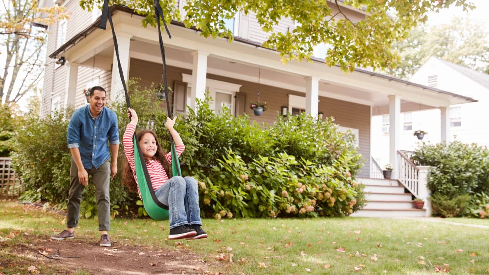 father pushing daughter on a swing outside of their home