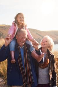 Grandfather giving granddaughter a ride on his shoulders while walking on a trail with her grandmother.