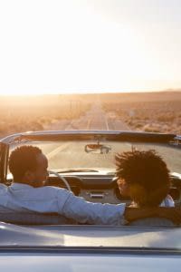 Couple in a convertible car with the top down driving at sunset.