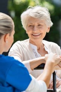 Nurse talking to an elderly patient sitting in a wheelchair outside.