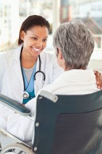 Long-Term Care Female Physician Smiles at and Comforts her Senior Patient in a Wheelchair