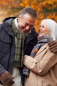 Senior couple embracing while walking on a woodland path in the Autumn.