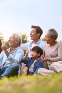 Multigenerational Asian family taking a selfie while sitting on the grass.