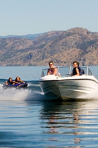 Man and woman in a boat on a lake with two kids on a tube