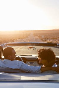 Man and woman in a car driving at sunset and looking at one another