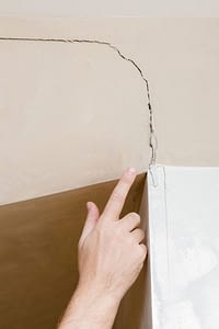 A hand pointing at a large crack in a tan wall