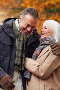 Senior couple embracing while walking on a woodland path in the Autumn.