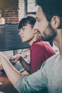 Two individuals looking at a computer screen displaying lines of code.